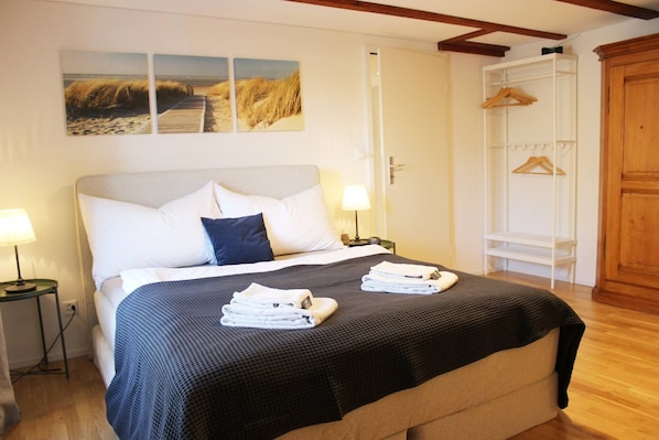 A neatly made bed with a dark quilt, a bedside table with a lamp, and a wooden wardrobe.