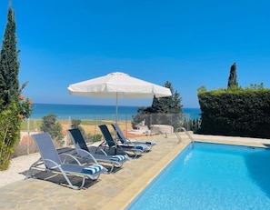 A poolside area with lounge chairs and an umbrella, overlooking a beach and the sea. - Spacious Luxury Private Sea View Villa (Argaka)