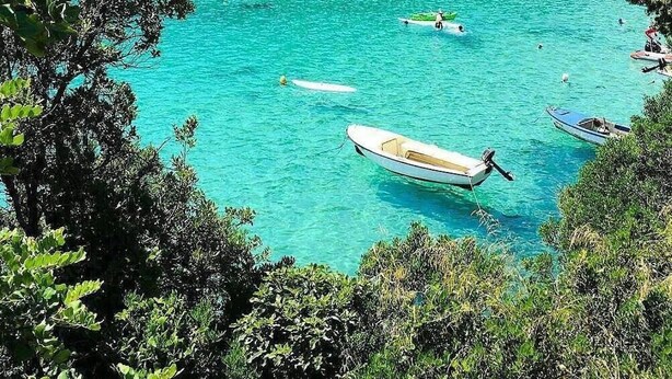Zona costera con aguas turquesas cristalinas, embarcaciones y una playa.