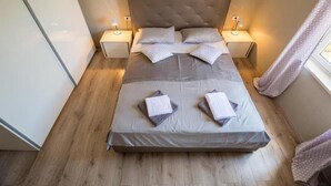 Una cama bien hecha con un cabecero capitonado, dos mesitas de noche con lámparas y una ventana con cortinas.