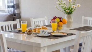 Una mesa de desayuno servida con frutero, un florero y un vaso de jugo de naranja.