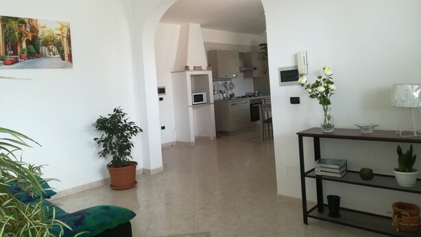 A spacious living area with a kitchen in the background, a dining table, and a potted plant. - Bright Apartment a few km From the sea (Minervino di Lecce)