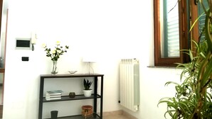 A room with a black console table, a white radiator, a window with blinds, and a potted plant. - Bright Apartment a few km From the sea (Minervino di Lecce)