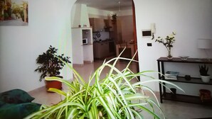 A living room with a large plant, a sofa, and a dining area visible through an archway. - Bright Apartment a few km From the sea (Minervino di Lecce)