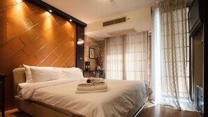 A neatly made bed with a headboard, a bedside table, and a large window with curtains. - 2A - 2 Bedroom Downtown Apartment With Shared Pool (Bangkok)
