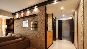 A modern living room with a sofa, a stone-patterned wall, and a wooden cabinet. - 2A - 2 Bedroom Downtown Apartment With Shared Pool (Bangkok)