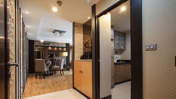 A modern kitchen with wooden cabinets, a dining area with chairs, and a visible ceiling light fixture. - 2A - 2 Bedroom Downtown Apartment With Shared Pool (Bangkok)