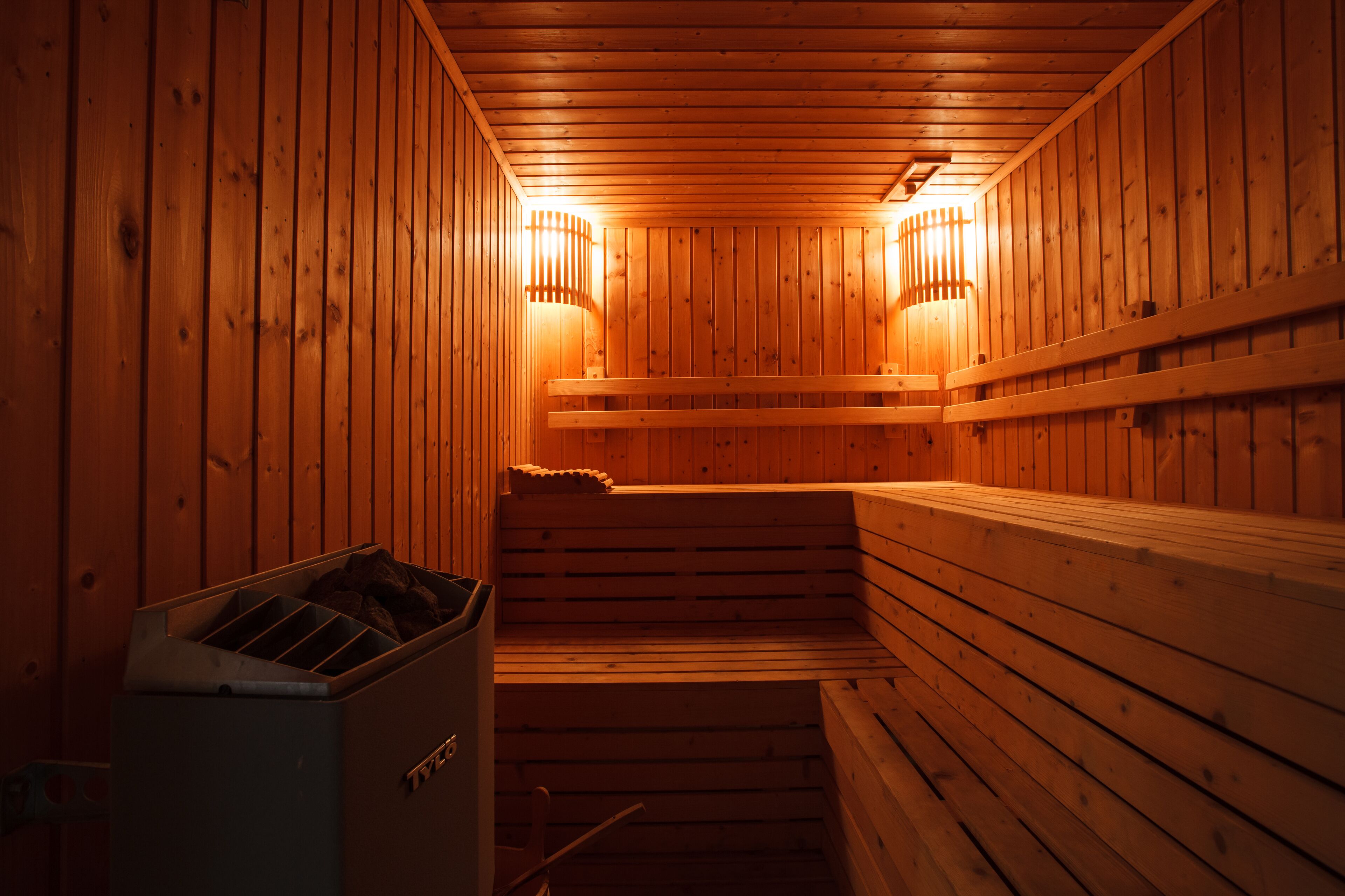 A sauna with wooden walls and benches, equipped with two wall-mounted lights.