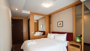 A hotel room with a large bed, a wooden nightstand, a mirror, and a framed picture on the wall. - 3A - 2 Bedroom Downtown Apartment With Shared Pool (Bangkok)