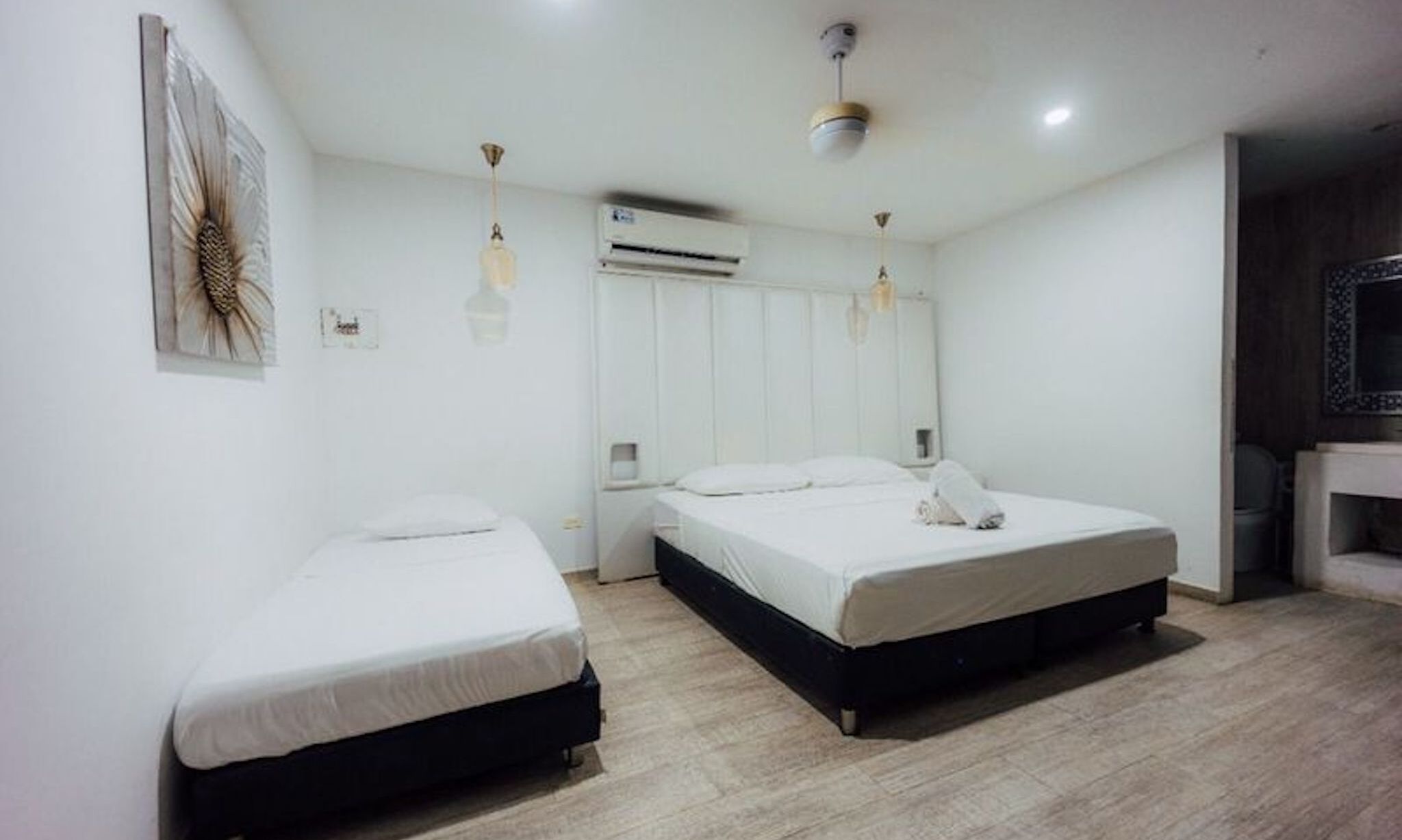 A hotel room with two single beds, a small bedside table, a mirror, an air conditioning unit, and a ceiling fan.