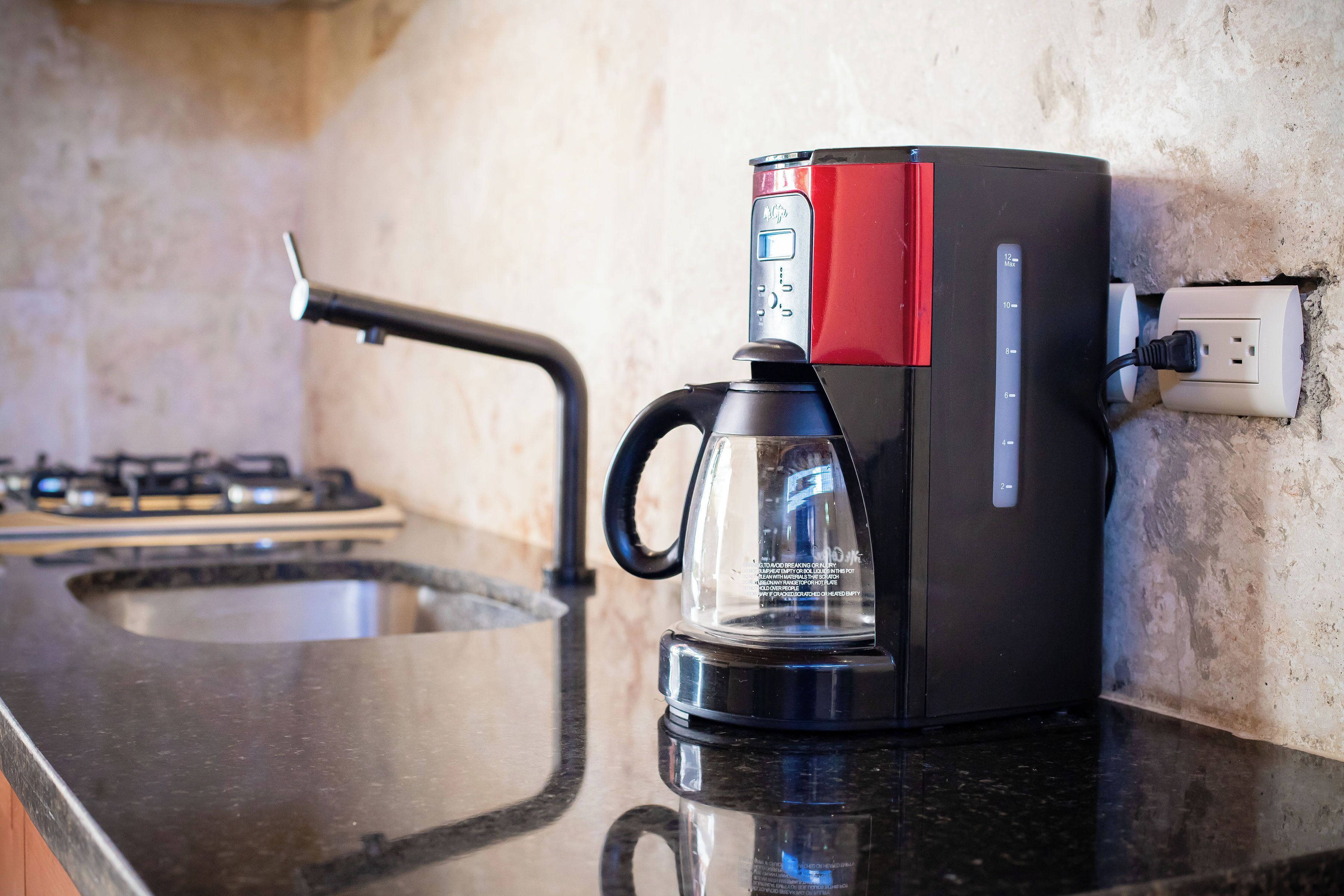 A coffee maker on a kitchen counter with a gas stove in the background.