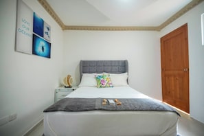 A bedroom with a bed, a nightstand, a wooden door, and wall art. - Room-central 1bd and Bth With Common Pic (Sosúa)