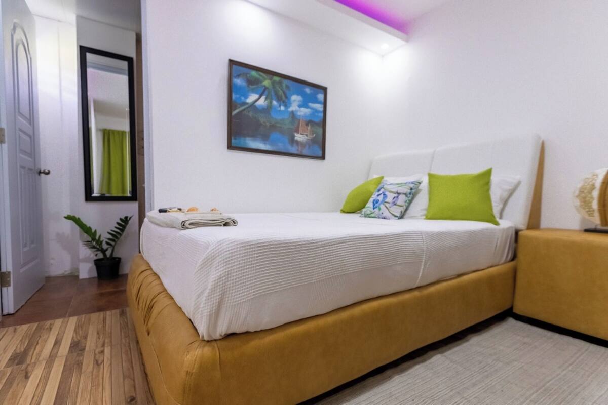 Un dormitorio con cama, un cuadro, una planta en maceta y una puerta.