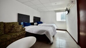Een hotelkamer met twee bedden, een bank, een witte tafel en een raam met uitzicht op de stad.