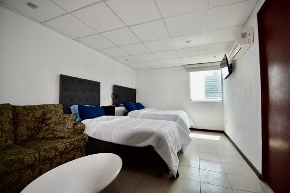 A hotel room with two beds, a sofa, a white table, and a window with a city view. - Habitacion Tipo Hotel En Obispado (Monterrey)