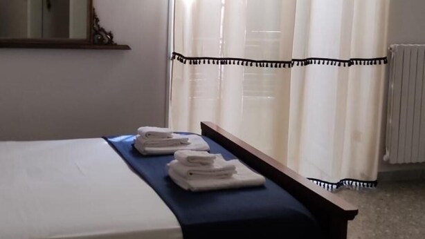A hotel room with a bed, a bedside table with towels, a mirror, and a window with sheer curtains. - Room-come and Visit Naples !! We Look fo (Naples)