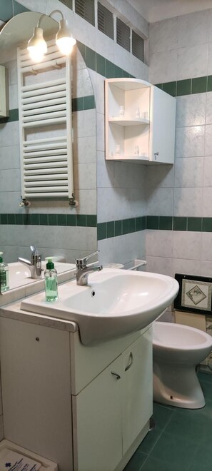 Un bagno con lavandino bianco, specchio e portasciugamani.