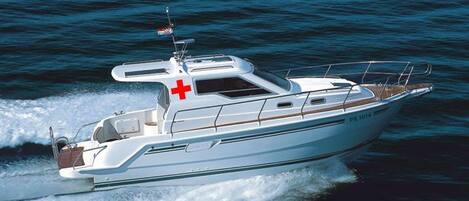Un bateau à moteur blanc, orné d’une croix rouge sur la cabine, d’un drapeau sur le mât et portant le numéro d’immatriculation « PR 1014 ».
