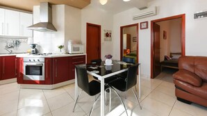 A compact kitchen with a central island, a dining area with a glass table and black chairs, and a brown leather sofa in a living area. - Nearby Beach, Modern Apartment Arena (Preko)