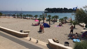 A beach with a pebble surface, umbrellas, and people relaxing. - Nearby Beach, Modern Apartment Arena (Preko)