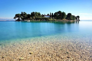 A clear view of a pebble beach leading to a small island with trees and a building.