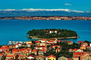 A coastal town with a prominent island, a marina, and a mountain range in the background.