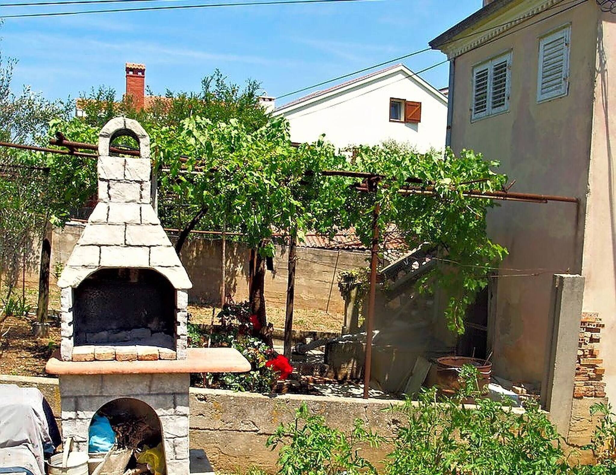 A stone-built outdoor oven in a garden with a white house in the background.