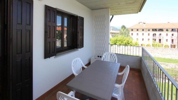 A balcony with a table and chairs, a window with shutters, and a view of buildings in the background. - Charming Apartment in Cividale del Friuli (Cividale del Friuli)