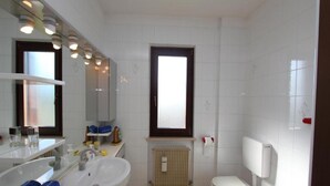 A bathroom with a white sink, mirror, and toilet. There is a window above the toilet and a radiator below it. - Charming Apartment in Cividale del Friuli (Cividale del Friuli)