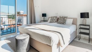 A modern hotel room with a large bed, a balcony with chairs, and a view of the city. - Sanders White Mountains - Charming Villa With Pool (Tremithousa)