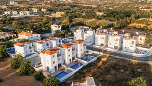 A residential area with modern white buildings, a swimming pool, and a hilly landscape in the background. - Sanders White Mountains - Charming Villa With Pool (Tremithousa)