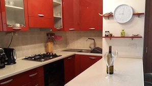 A kitchen with red cabinets, a white countertop, a gas stove, a sink, and a wine glass on the counter. - 3 Bed Apt loc Marinella Pizzo Vv 89812 Calabria, Southern Italy (Pizzo)