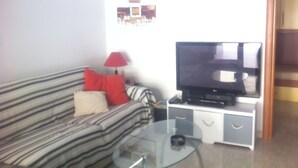 A living room with a striped sofa, a glass coffee table, a TV on a white cabinet, and a red lamp. - 3 Bed Apt loc Marinella Pizzo Vv 89812 Calabria, Southern Italy (Pizzo)