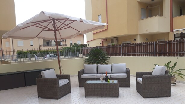 An outdoor patio area with wicker furniture, a white umbrella, and a tiled floor. - 3 Bed Apt loc Marinella Pizzo Vv 89812 Calabria, Southern Italy (Pizzo)
