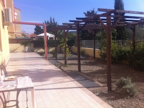 Un espace patio agrémenté d’une pergola, d’un chemin pavé et d’une table avec un set de table.