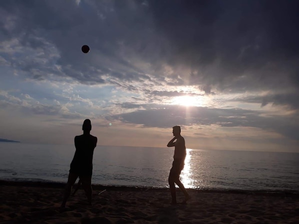 Deux personnes jouent à la balle sur une plage au coucher du soleil.