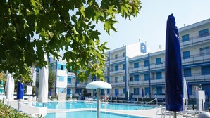 A swimming pool with lounge chairs and umbrellas, surrounded by a building with multiple balconies. - Feel at Home in our Accommodation - Beahost (Caorle)