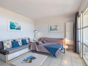 A modern, well-lit room with a sofa, a bed, and a coffee table. There are two framed artworks on the walls and a lamp on the side table. - Les Bastides (O4 259) by Interhome (Agay Village Cap Esterel)
