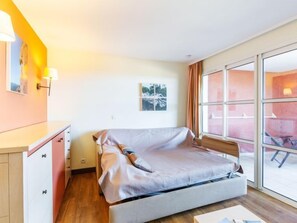 A bedroom with a bed, a nightstand, a mirror, and a window with a view of the outside.