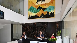 Ein Empfangsschalter mit einem Schild, das "ENRISE by SAISE" zeigt, in einer modernen Lobby mit Marmorboden und einem großen Gemälde über dem Schalter.