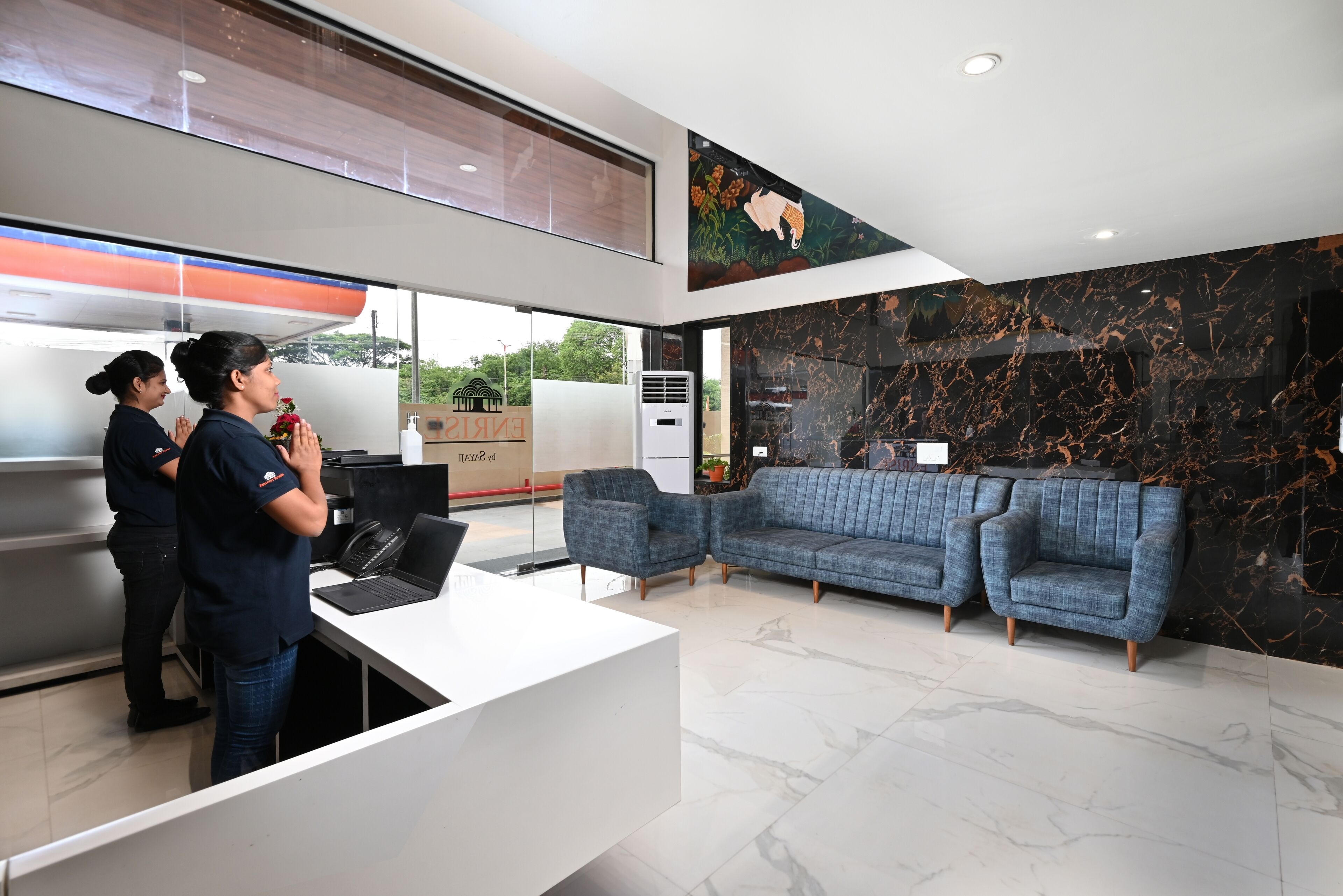 A modern reception area with a white desk, two sofas, and a large mural on the wall.
