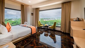 Ein Hotelzimmer mit einem Bett, zwei Stühlen, einem kleinen Tisch und großen Fenstern mit Blick auf die Stadt.