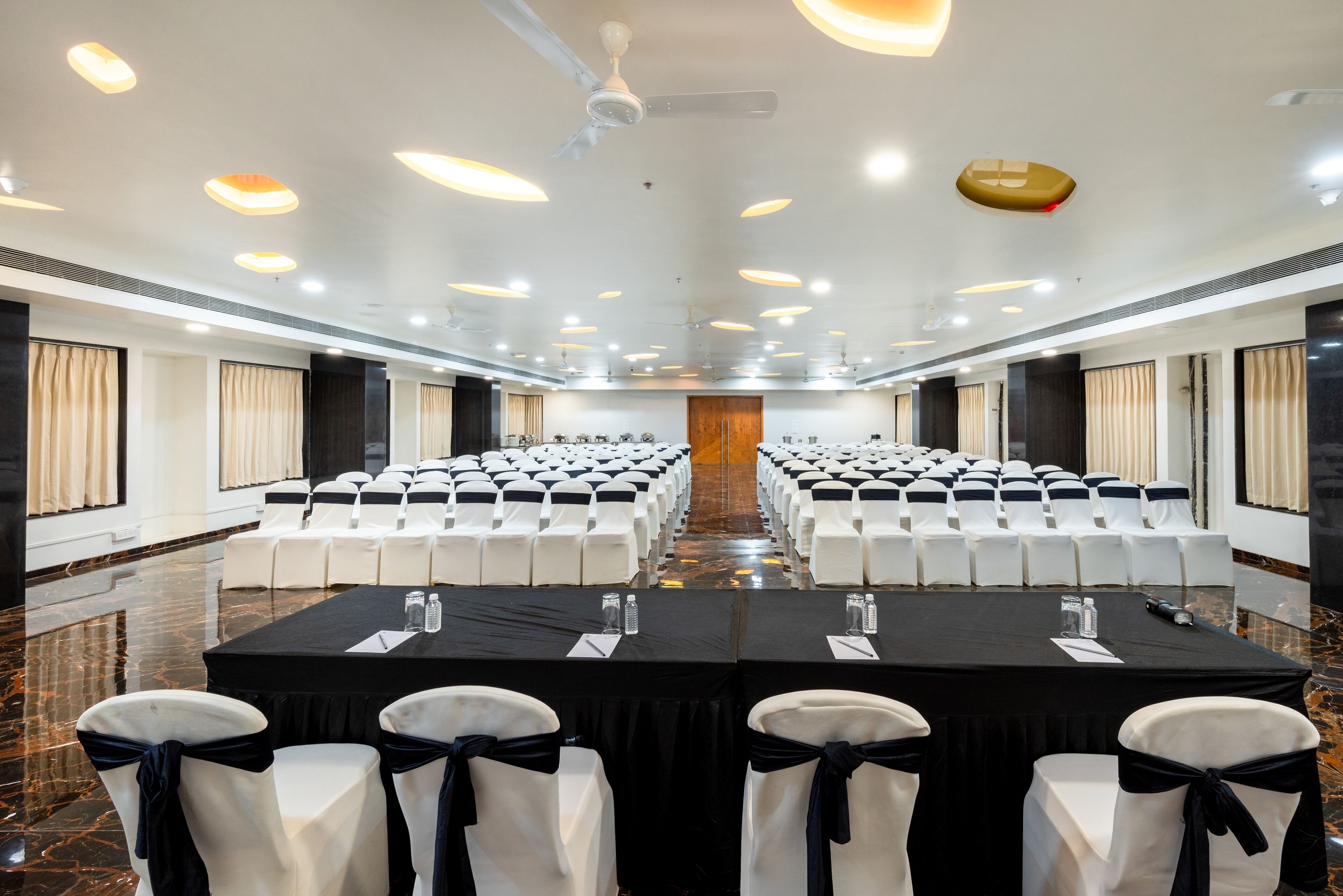 A conference room with rows of white chairs, black tablecloths, and a central podium.