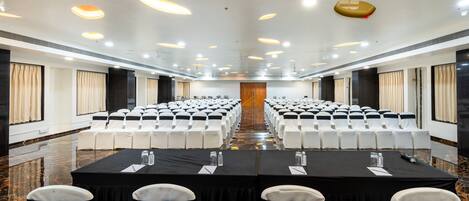 A conference room with rows of white chairs, black tablecloths, and a central podium.