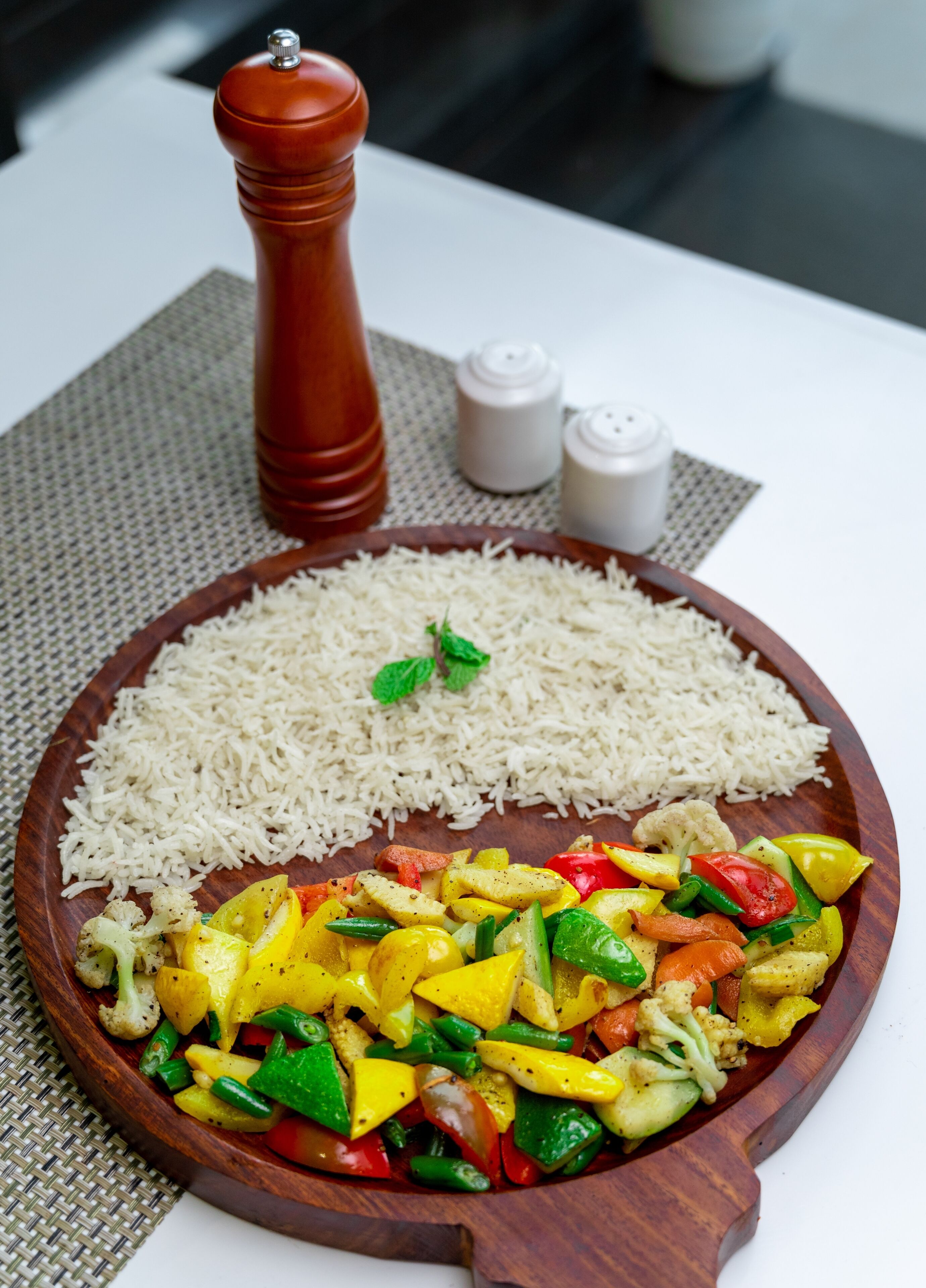 A wooden plate with white rice and a colorful vegetable stir-fry.
