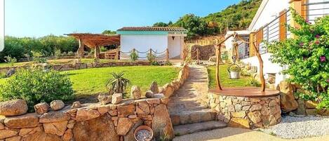 A stone pathway leading to a rustic house with a small garden and a gazebo.