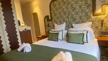 Une chambre d’hôtel avec un grand lit, une couvre-lit verte et des oreillers assortis. On y trouve une table de chevet avec une lampe, un miroir et une petite table.