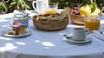 Une table de petit-déjeuner installée à l’extérieur, avec une variété d’aliments, notamment du pain, des fruits et des boissons.