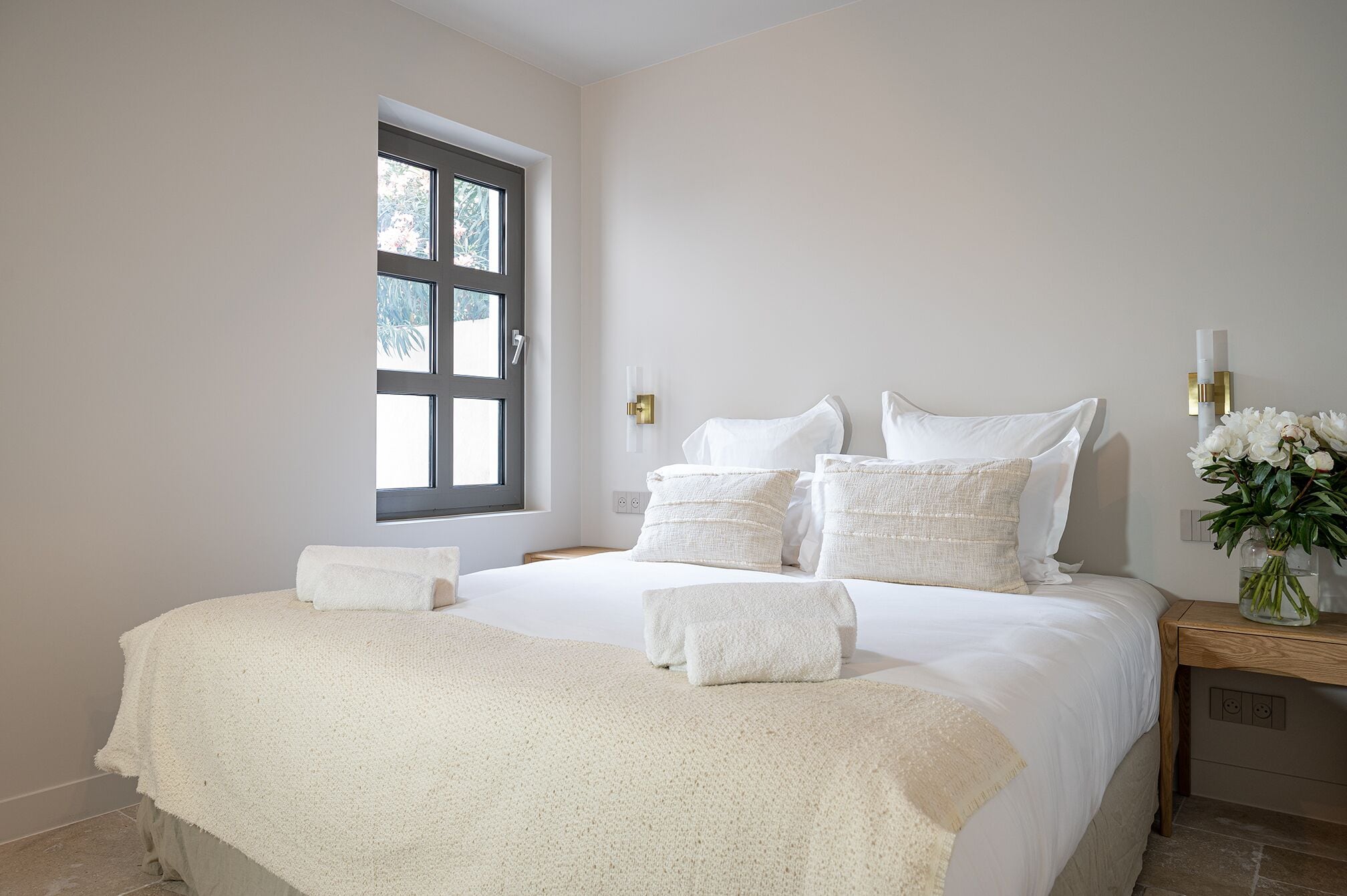 Een slaapkamer met een groot bed, een raam en een nachtkastje met een bloevas.