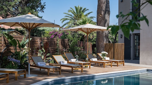 Un espace aménagé au bord de la piscine, avec des chaises longues et des parasols, entouré d’une terrasse en bois et d’un mur en briques.